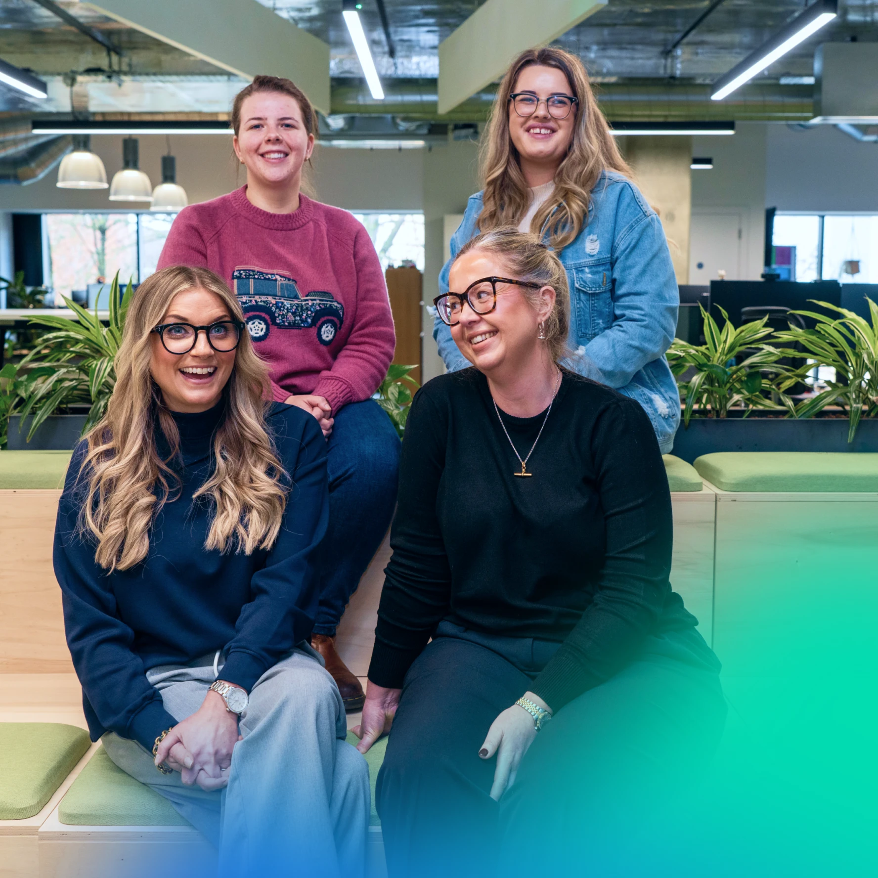 Four women in an office looking at the camera and laughing