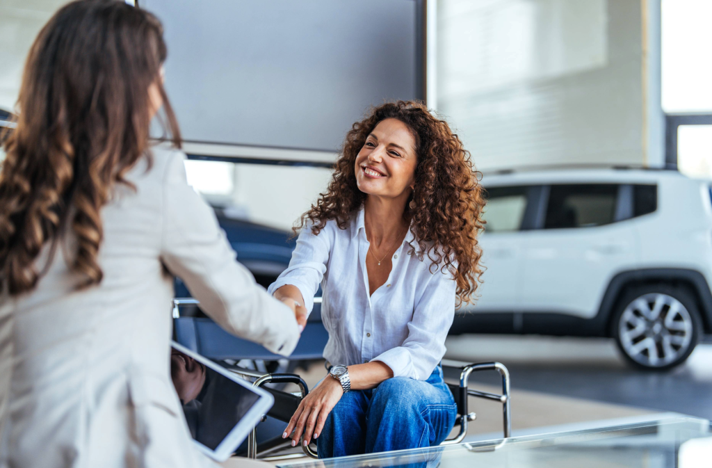 two women shaking hands in a car dealership