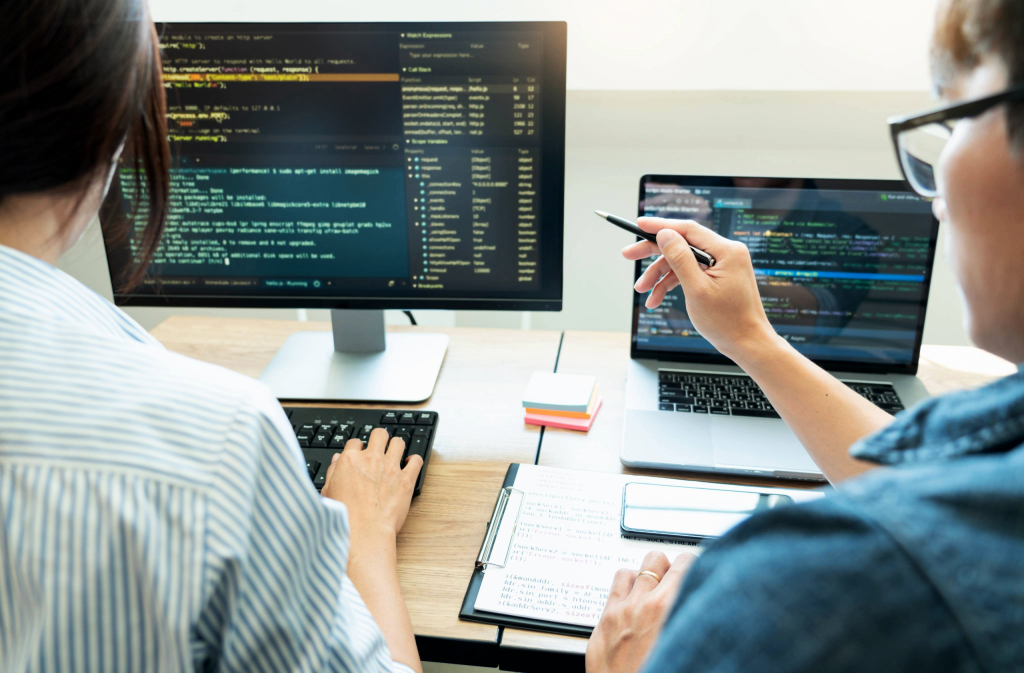 man and woman looking ad code on a computer in an office