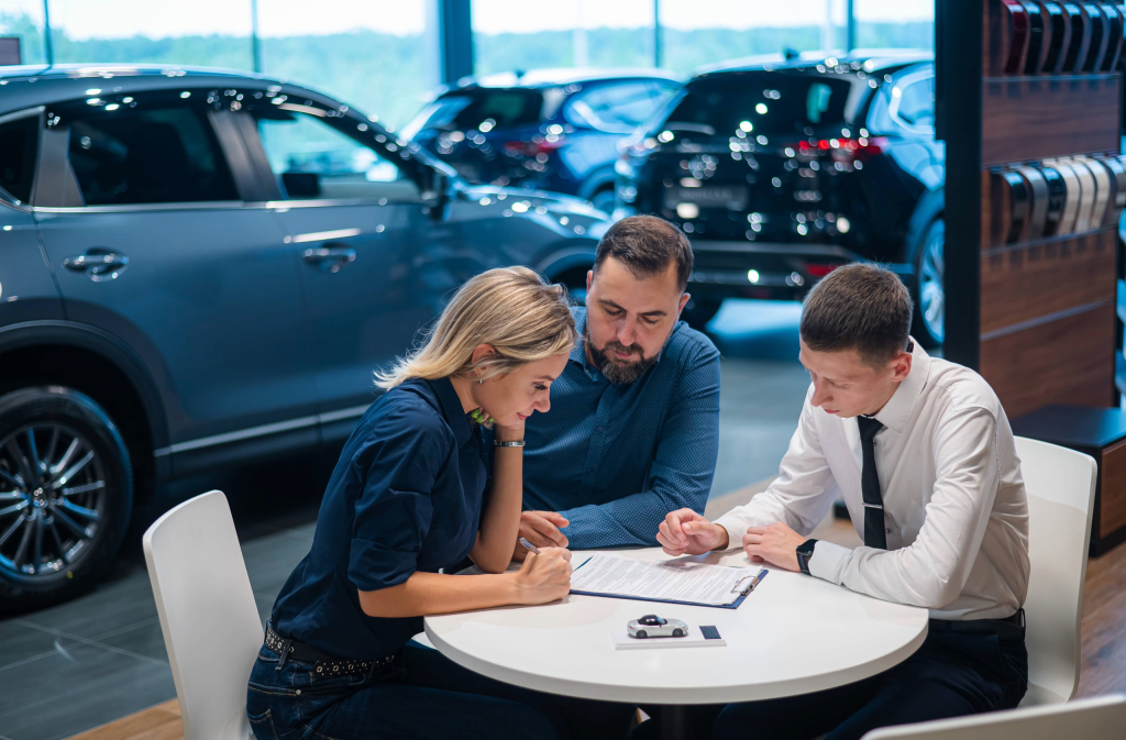 couple speaking to a salesman in a car dealership around a table