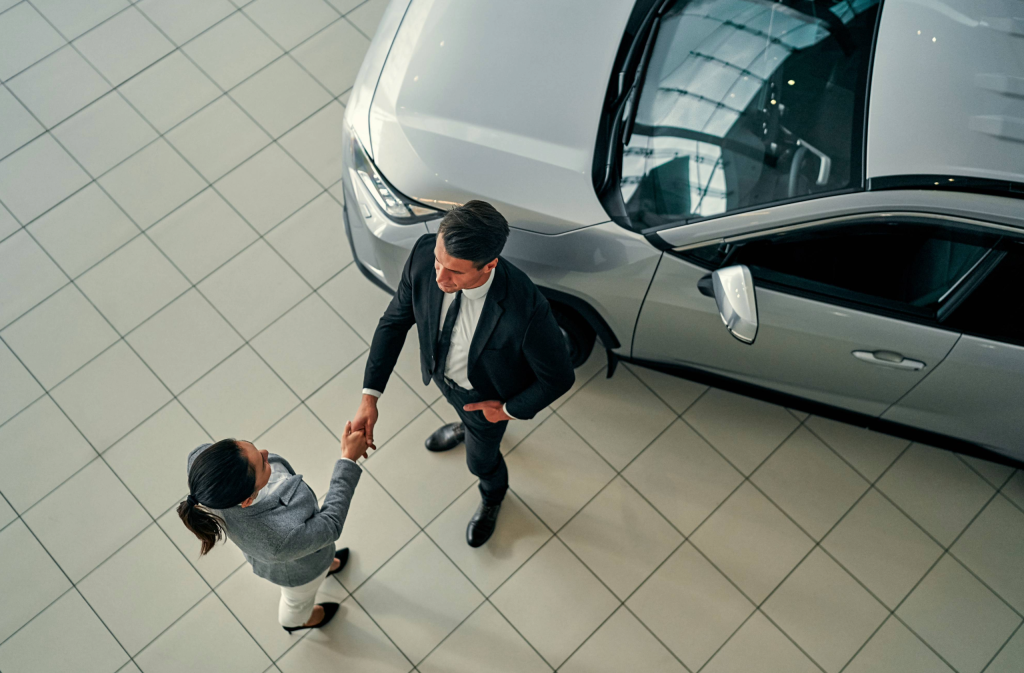 man and woman shaking hands in a car dealership